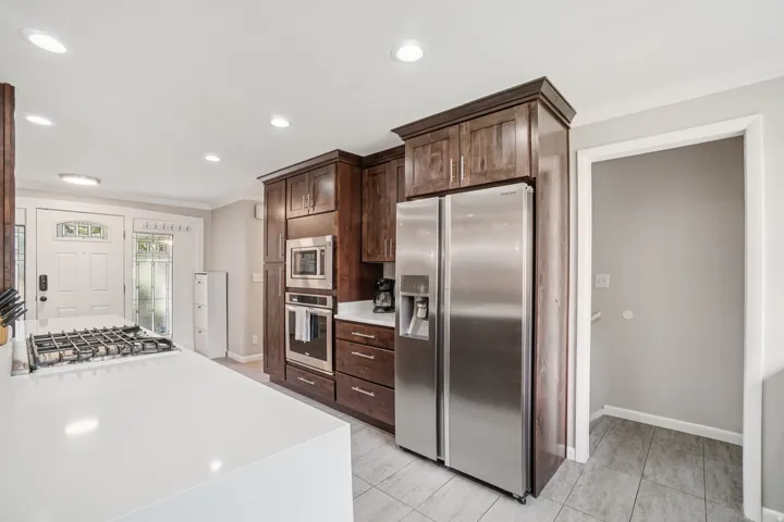 Spacious kitchen featuring an island with a built-in gas cooktop, stainless steel appliances, rich wood cabinetry, light-toned countertops, and tiled flooring