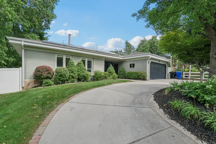 Expansive driveway with brick edging, attached garage with a dark door, and a white privacy fence