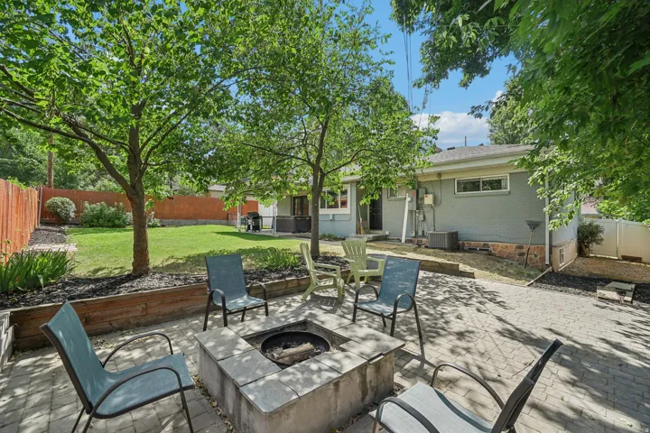 Expansive backyard featuring a stone paver patio, a built-in fire pit, a manicured lawn, and mature trees