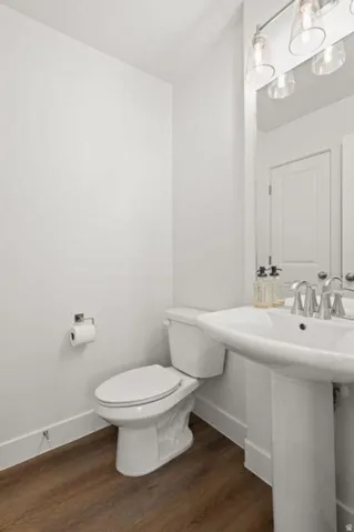 Pedestal sink with chrome fixtures, white toilet, and wood-finish flooring