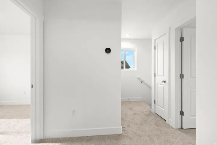 Carpeted hallway with white walls, white trim, and a white interior door
