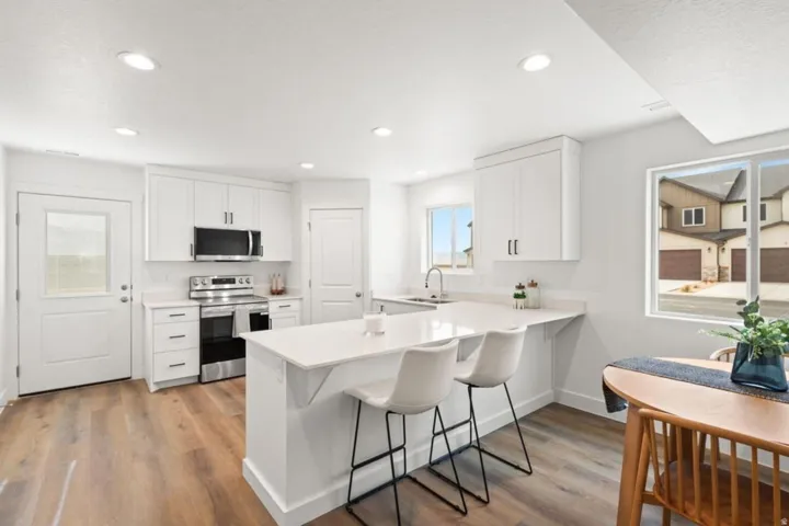 Modern kitchen featuring white cabinetry, stainless steel appliances, wood-finish flooring, recessed lighting, and a kitchen island with seating