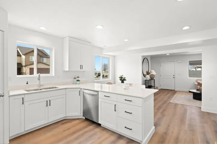 Contemporary kitchen featuring white cabinetry, light-toned countertops, stainless steel appliances, and wood-finish flooring
