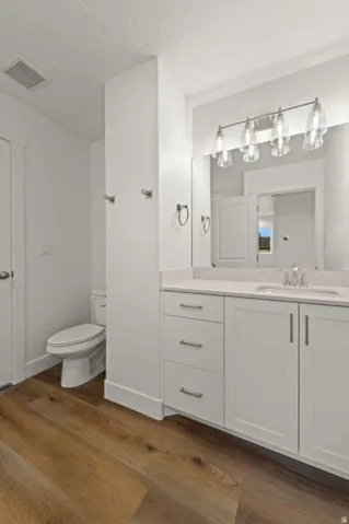 Wood-finish flooring complementing a white vanity with silver hardware, a neutral countertop, and a four-light fixture