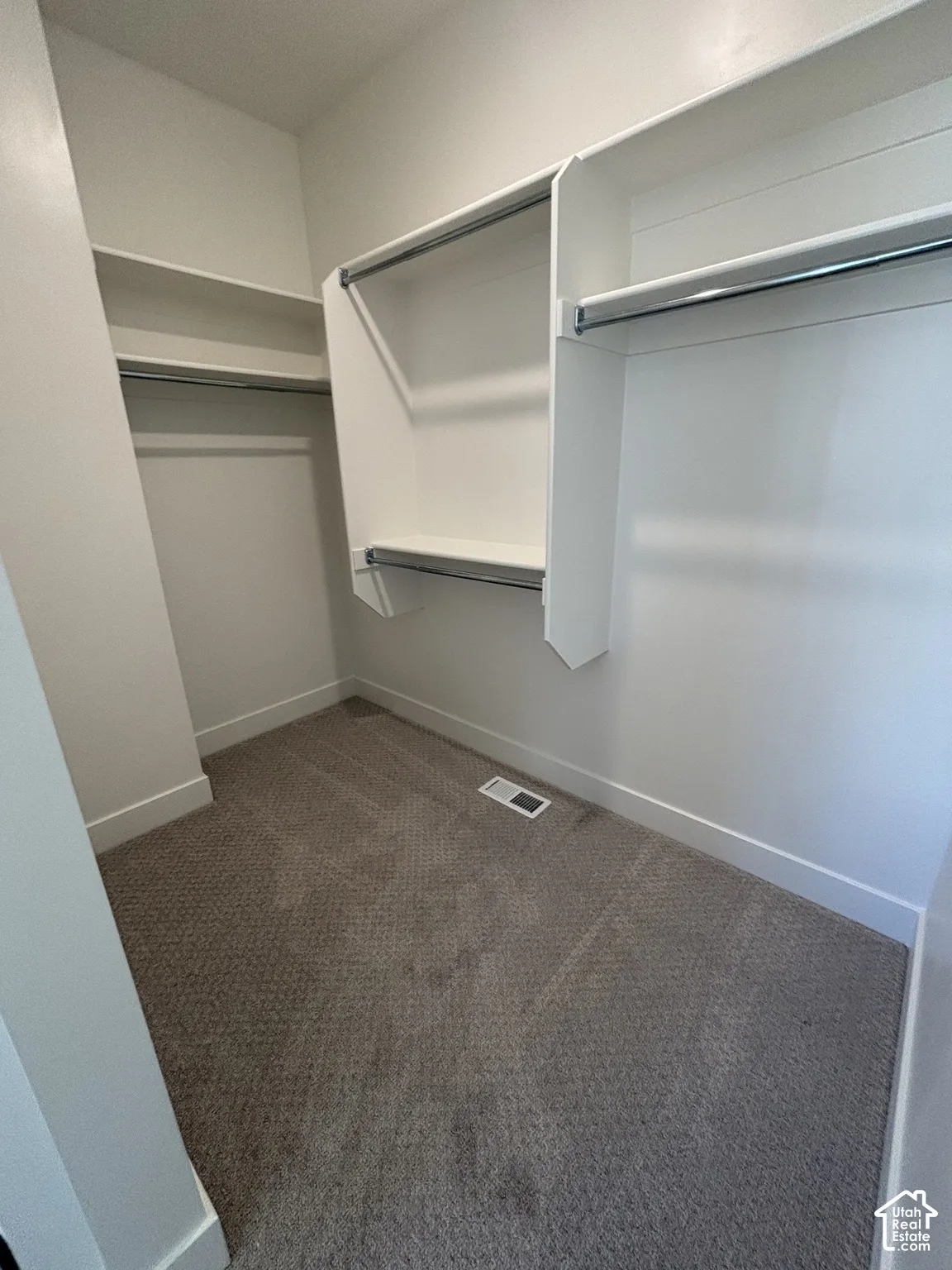Spacious closet with built-in shelving, chrome hanging rods, and neutral-toned carpeting
