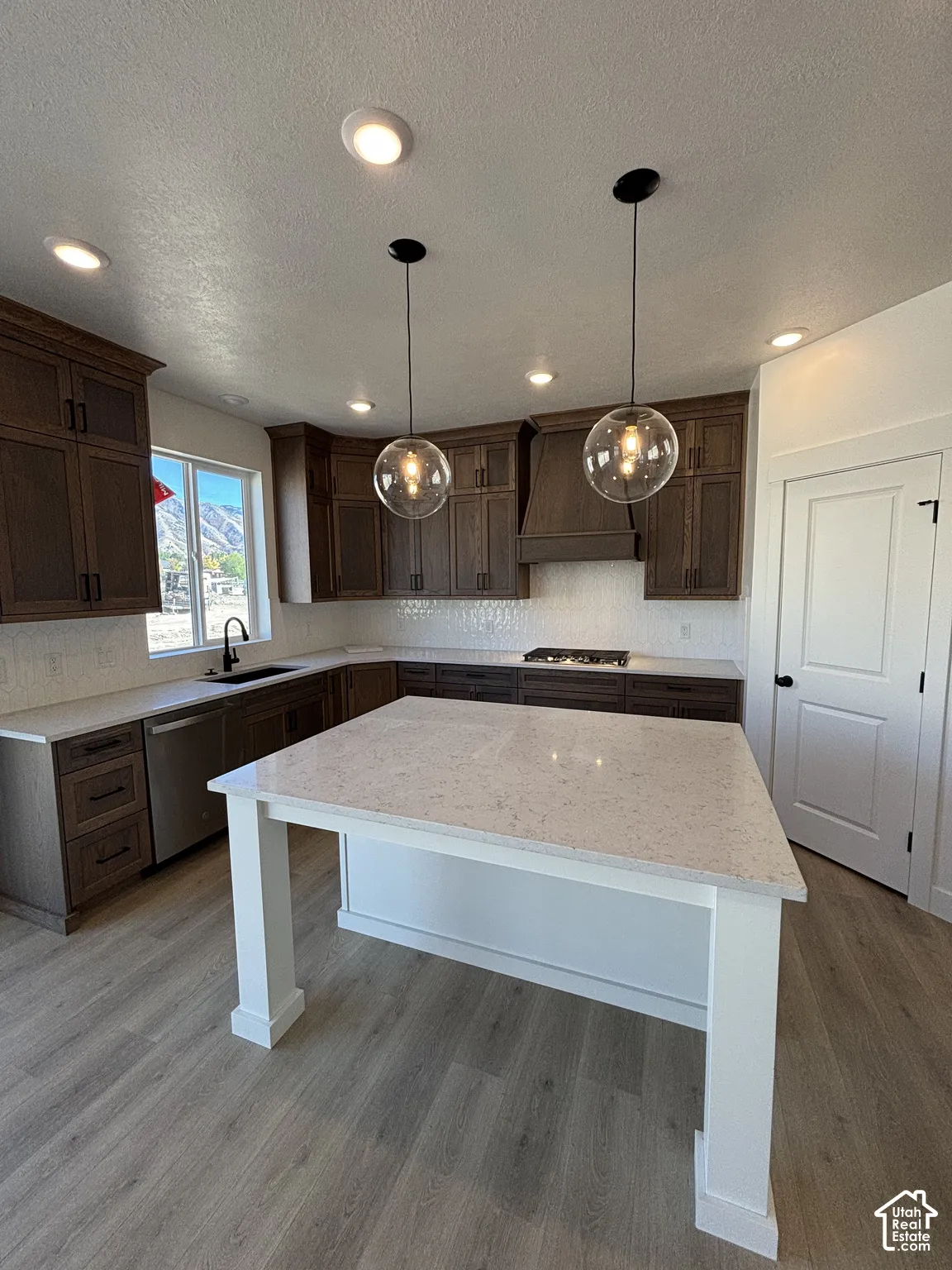 Kitchen featuring recessed lighting, two pendant lights, wood-finish flooring, a white countertop island, and dark wood cabinetry