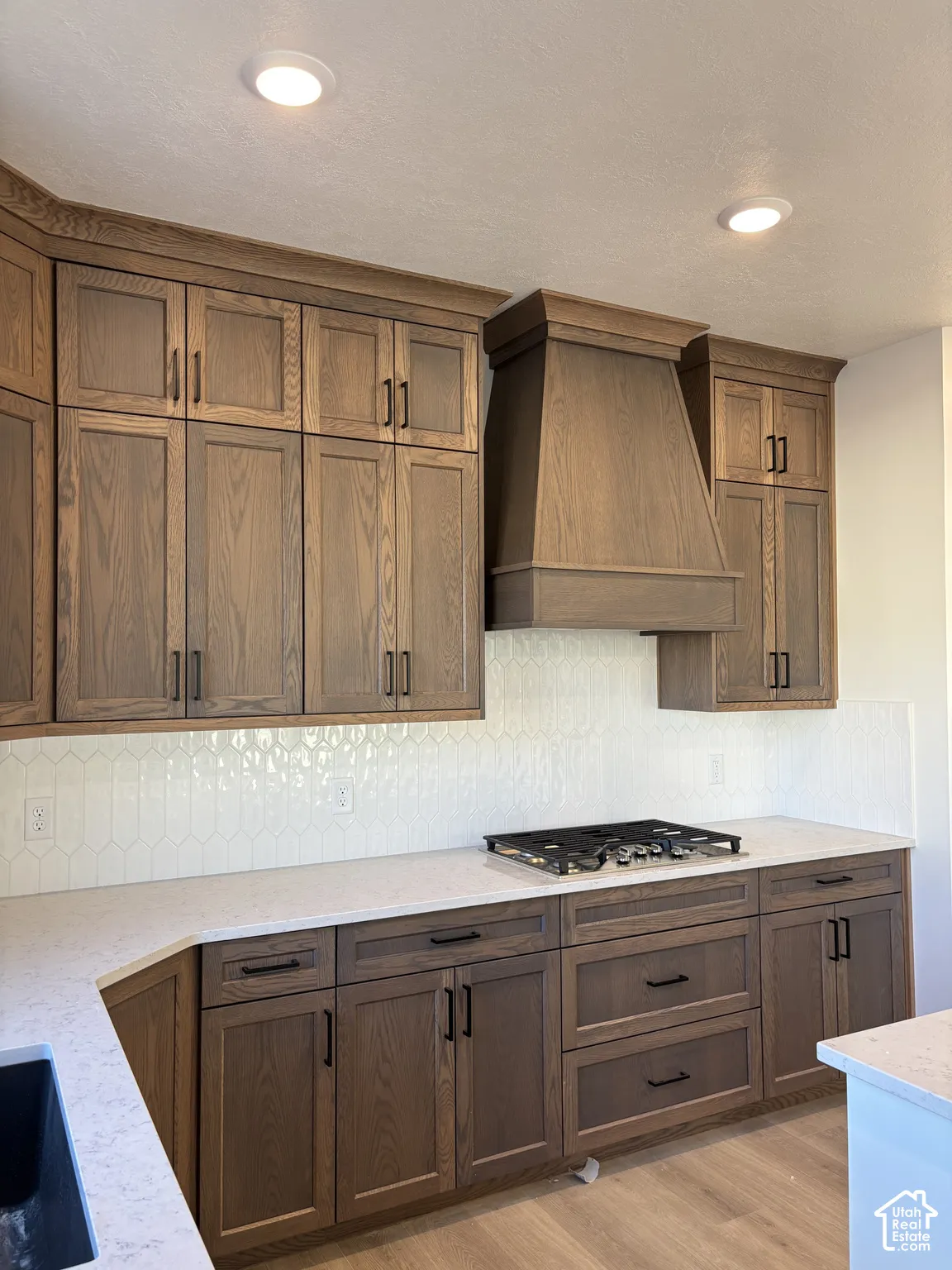 Recessed lighting illuminates wood-finish cabinetry, a built-in range, and a decorative range hood