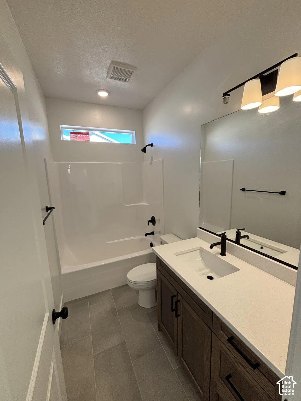 White bathtub with black fixtures, dark wood-finish vanity with white countertop, recessed sink with black faucet, large wall-mounted mirror, and gray tile flooring