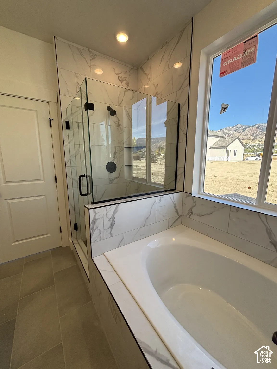 Spacious bathroom featuring a built-in soaking tub, a walk-in shower with glass enclosure, white and gray veined tile accents, and recessed lighting