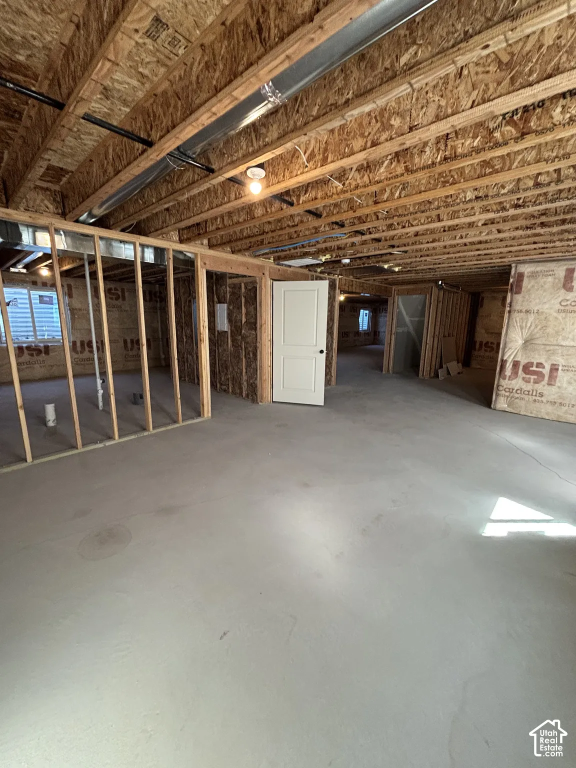 Unfinished interior with concrete flooring, exposed wood ceiling joists, framed interior walls, and an interior door