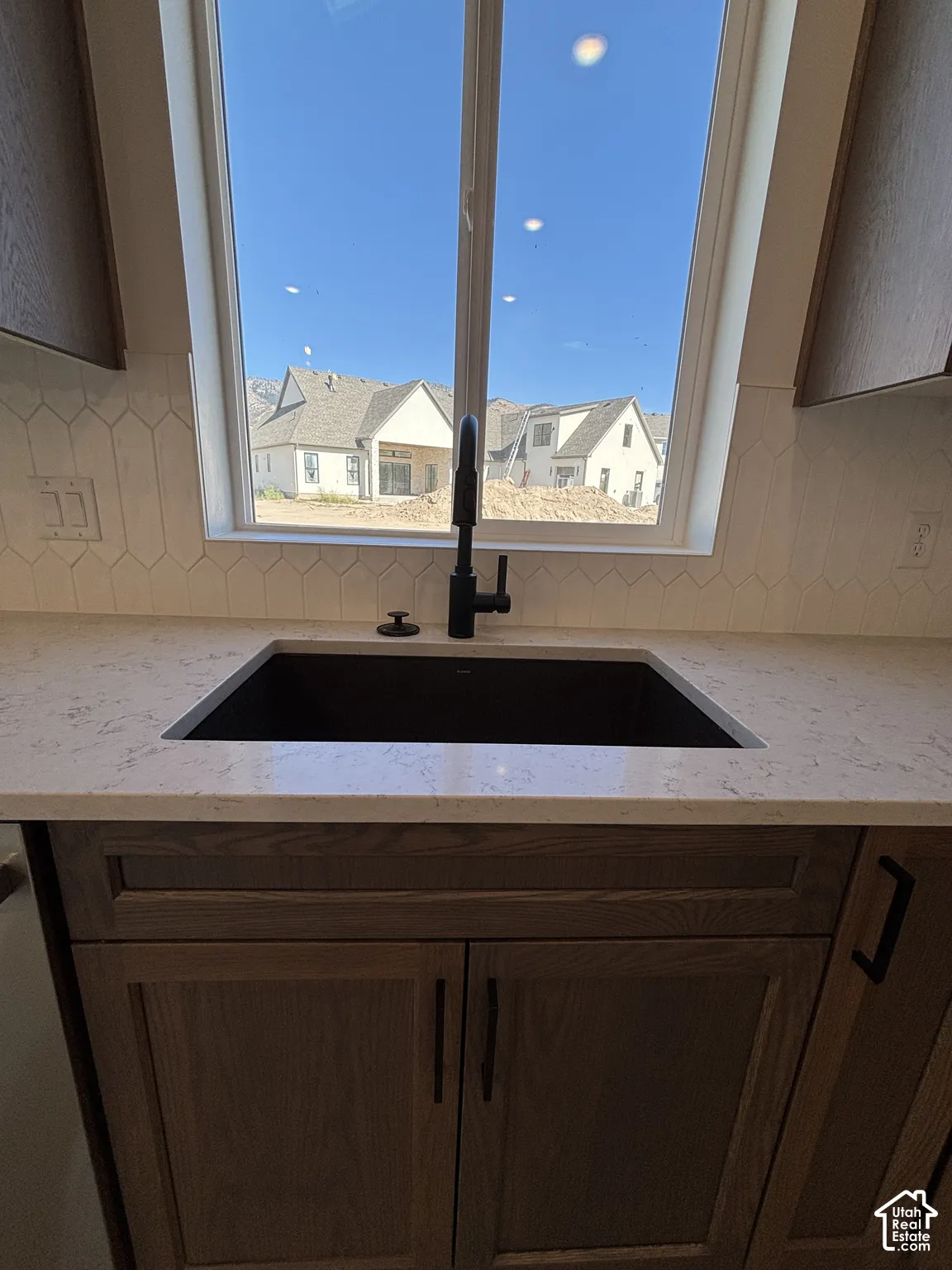 Black sink with a matte black faucet, light-toned countertop, wood-finish cabinetry, and white geometric backsplash