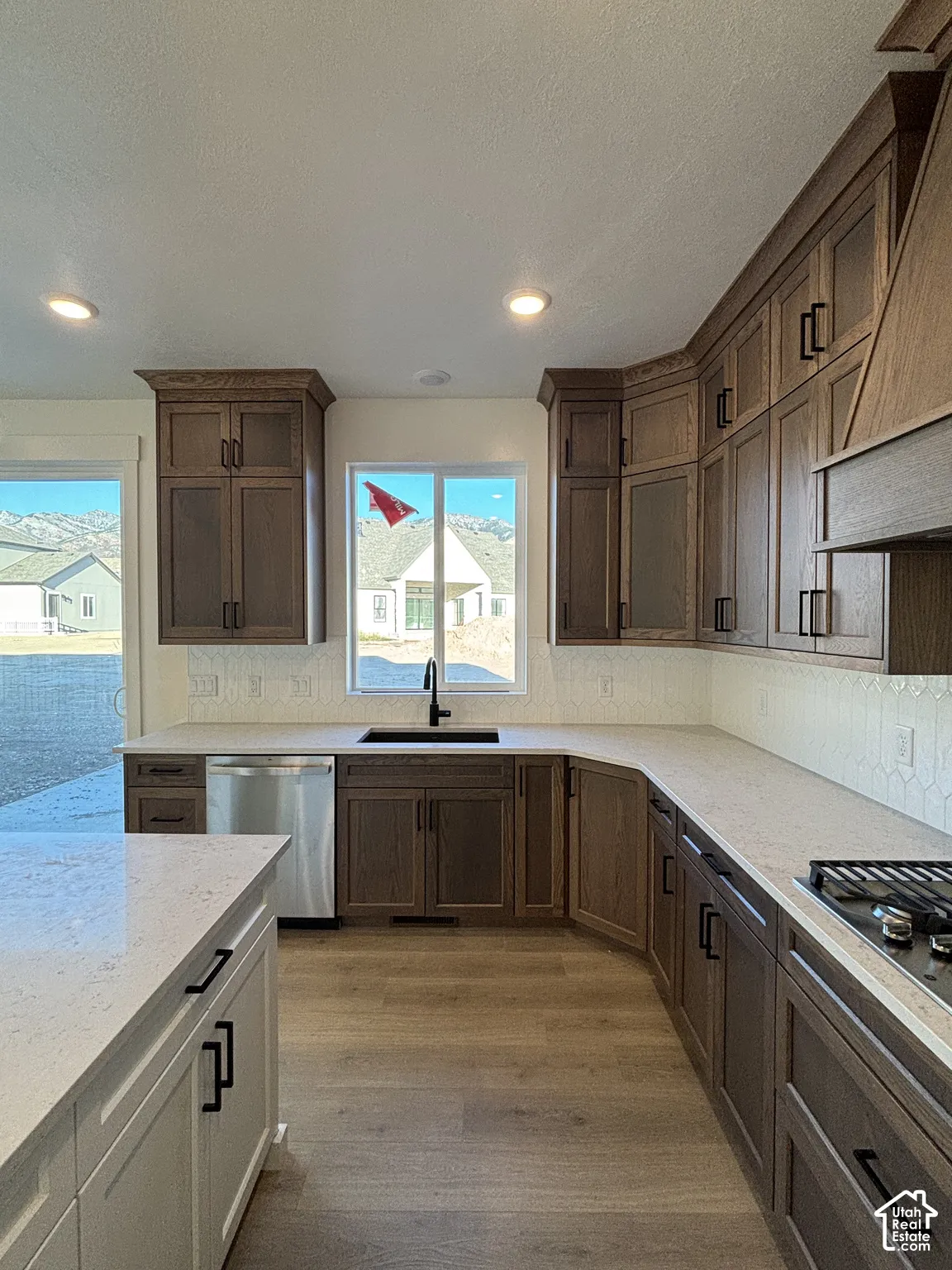 Kitchen featuring wood-finish cabinetry, light-toned countertops, and a full-size stainless steel dishwasher