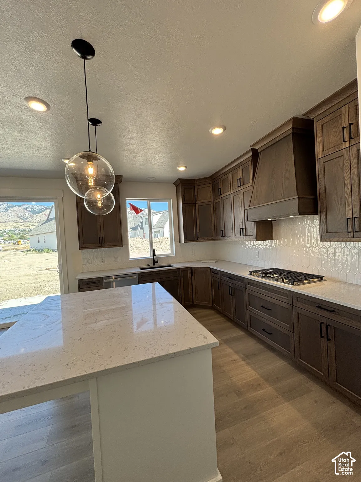 Kitchen featuring dark wood-finish cabinetry, light-toned countertops, a full-height tile backsplash, a gas range, and recessed lighting