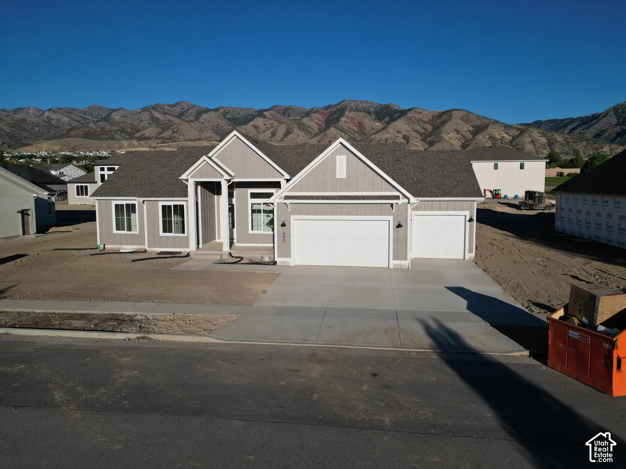 Mountain backdrop, light gray siding, dual garage doors, concrete driveway, and a covered entry