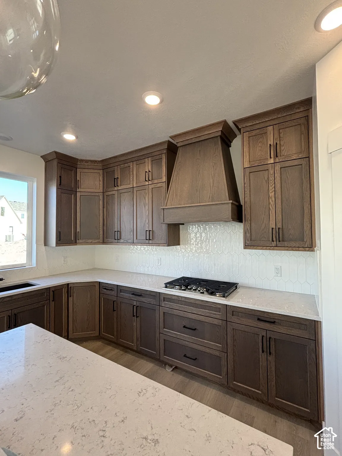 Wood-finish cabinetry with black hardware, white quartz countertops, gas cooktop, and a decorative tile backsplash