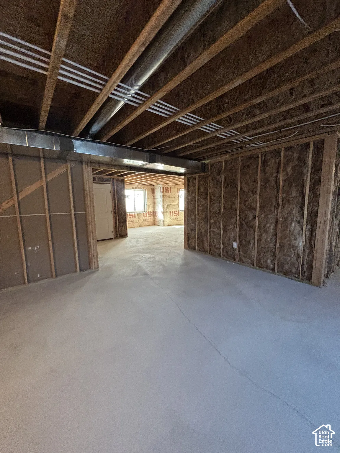 Unfinished basement space featuring exposed wood joists, concrete flooring, and insulated framed walls