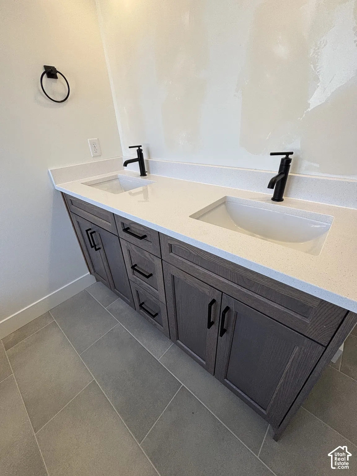 Dual vanity with integrated sinks, light-toned countertop, dark wood-finish cabinetry, matte black hardware, and tiled flooring