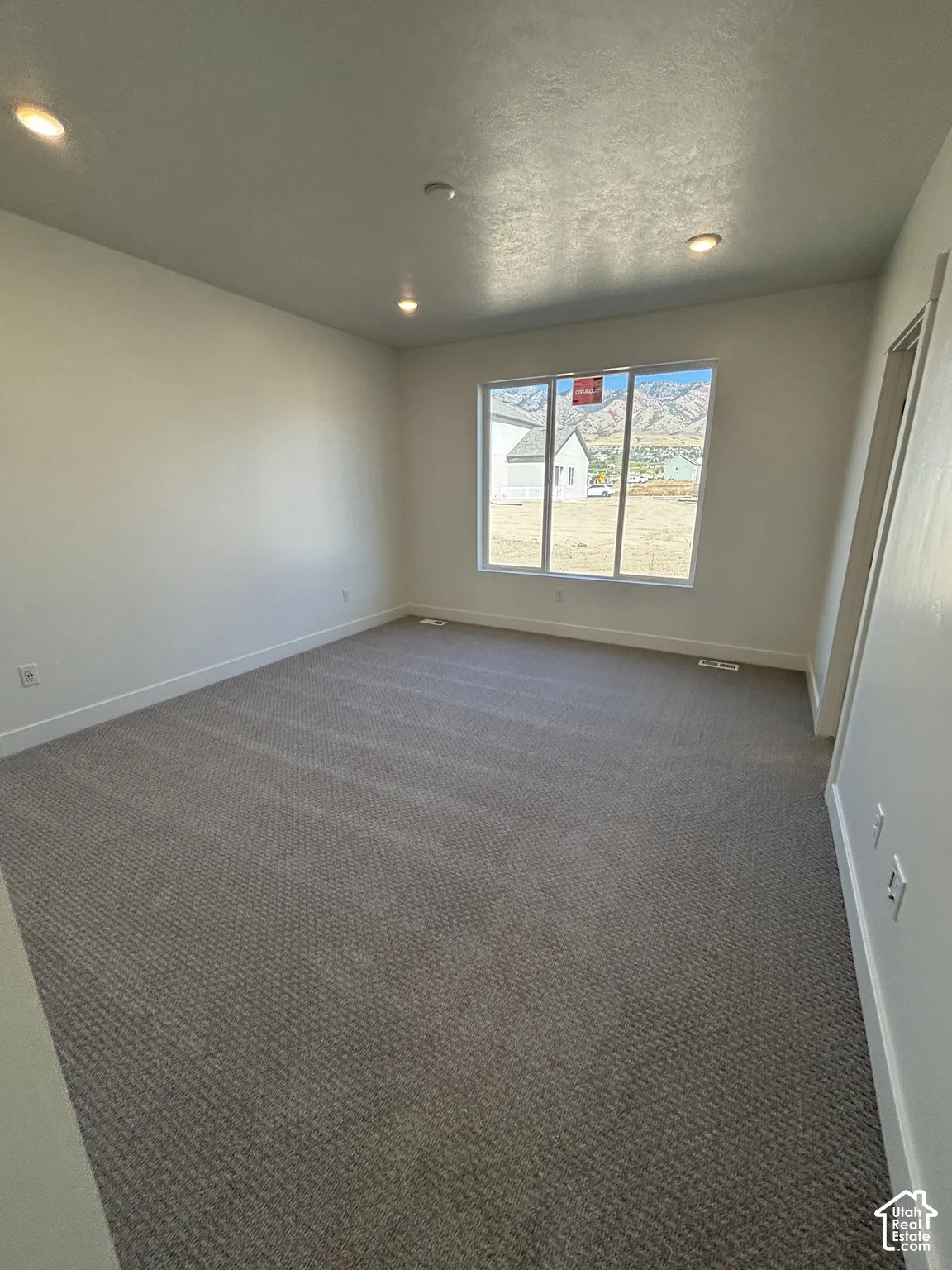 Recessed lighting, neutral wall paint, gray patterned carpeting, and a large window