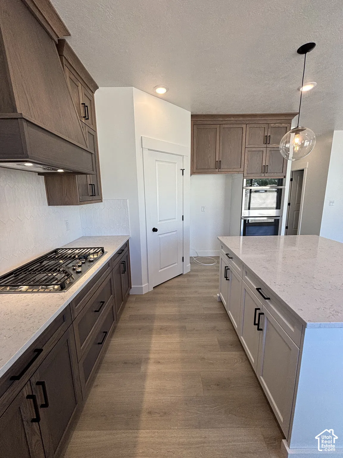 Well-appointed kitchen featuring wood-finish cabinetry, light-toned countertops, a built-in gas range, wood-finish flooring, and a pendant light fixture