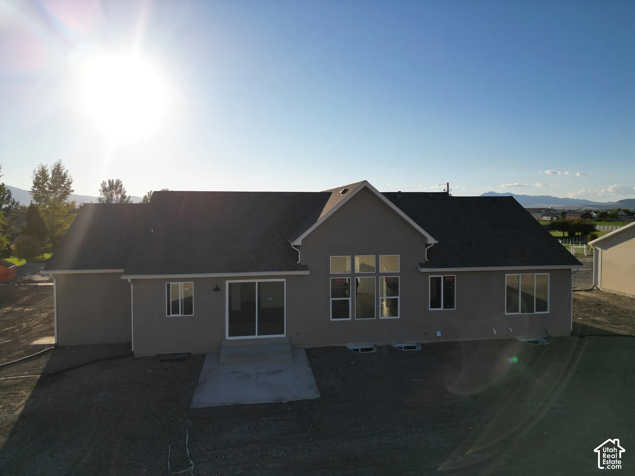 Rear facade featuring a concrete patio, multiple windows, and a dark shingle roof