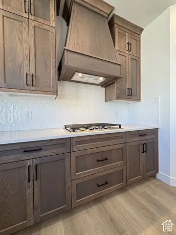 Wood-finish cabinetry with black hardware, white solid surface countertops, patterned tile backsplash, and wood-finish flooring