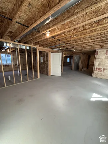 Unfinished interior with concrete flooring, exposed wood ceiling joists, framed interior walls, and an interior door