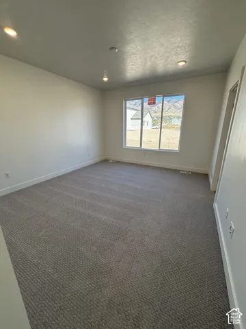 Recessed lighting, neutral wall paint, gray patterned carpeting, and a large window