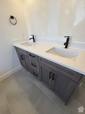 Dual vanity with integrated sinks, light-toned countertop, dark wood-finish cabinetry, matte black hardware, and tiled flooring