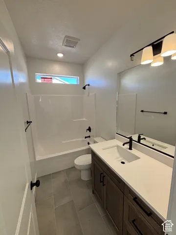 White bathtub with black fixtures, dark wood-finish vanity with white countertop, recessed sink with black faucet, large wall-mounted mirror, and gray tile flooring