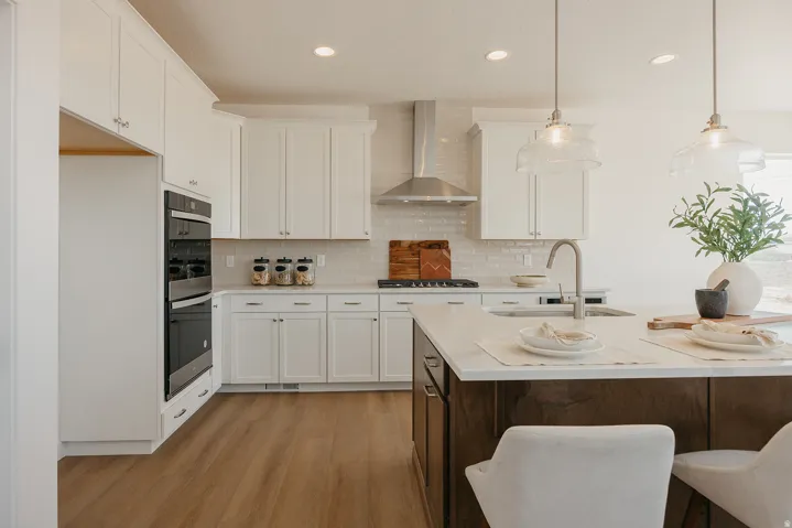 White cabinetry, stainless steel double wall ovens, wood-finish flooring, island with integrated sink, recessed lighting
