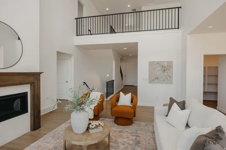 Spacious living area featuring a fireplace with wood mantel, a second-story interior balcony with black railing, light wood-finish flooring, and high ceilings