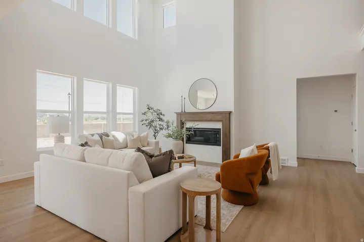 High ceilings with upper windows, wood-finish flooring, a fireplace with a wood mantle and white tile surround, and multiple tall windows