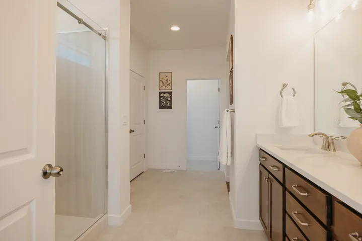 Walk-in shower with sliding glass door, single vanity with wood-finish cabinetry, light-toned countertop, and brushed nickel fixtures