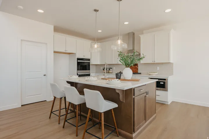 Kitchen featuring a large island with seating, pendant lighting, built-in double ovens, and wood-finish flooring