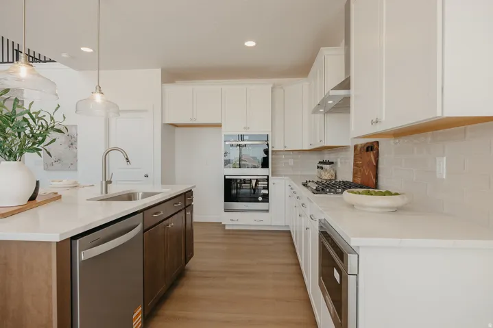 Kitchen featuring white cabinetry, light countertops, stainless steel appliances, wood-finish flooring, and a subway tile backsplash