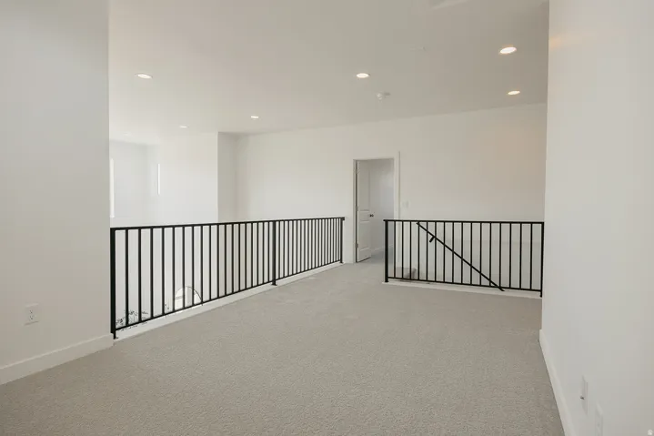 Carpeted loft space with recessed lighting and black metal railings