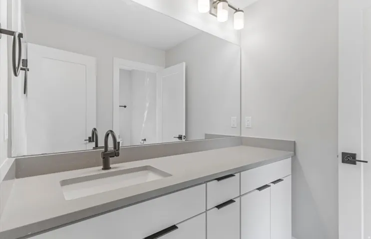 Modern bathroom vanity featuring an extended quartz countertop with integrated sink, matte black faucet, and white cabinetry with sleek hardware