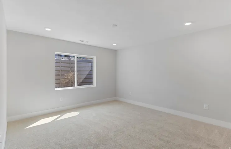Basement suite with recessed lighting, light-toned carpeting, white window trim, and neutral wall tones