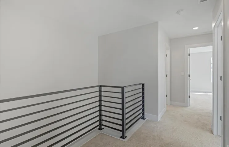 Contemporary horizontal rod railing, recessed ceiling lighting, light-toned carpeting, and white interior doors