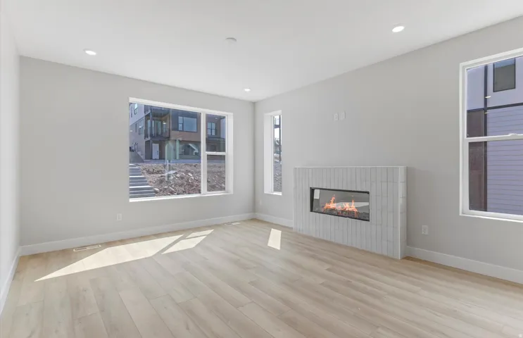 Recessed lighting, wood-finish flooring, a modern linear fireplace with a white tile surround, and multiple windows
