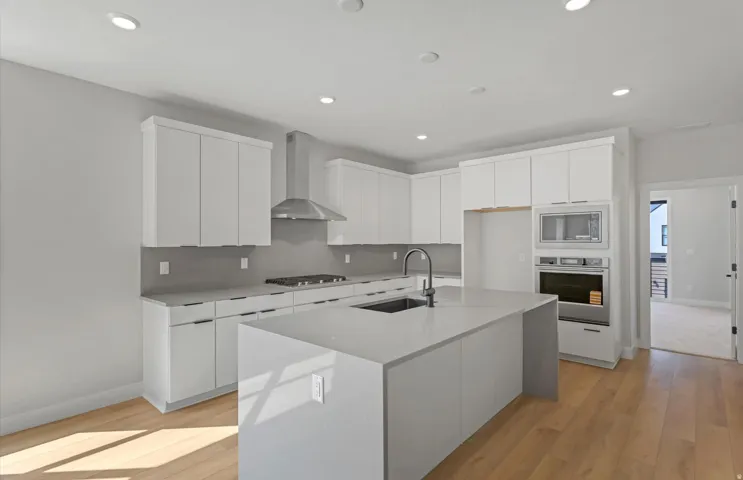 Modern kitchen featuring white cabinetry, a central island with an integrated sink, stainless steel appliances, and 3 pendant light pre-wires above island