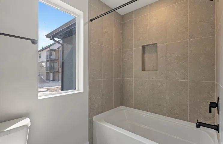 Rectangular bathtub featuring a tiled surround with an integrated niche, matte black fixtures, and a white window frame