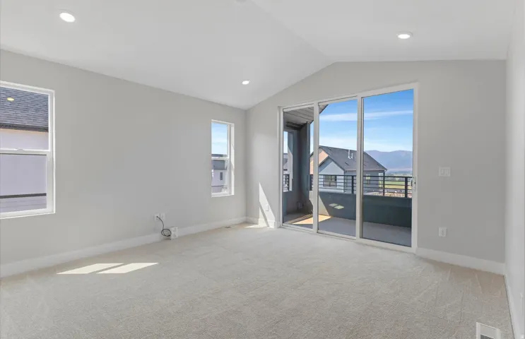 Upstairs loft featuring vaulted ceilings with recessed lighting, light-toned carpet, a private balcony with metal railing, and expansive sliding glass doors