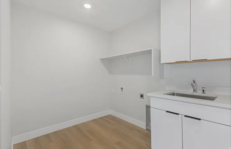 Laundry area featuring wood-finish flooring, recessed lighting, built-in shelving, white cabinetry, and a utility sink with a stone-finish countertop