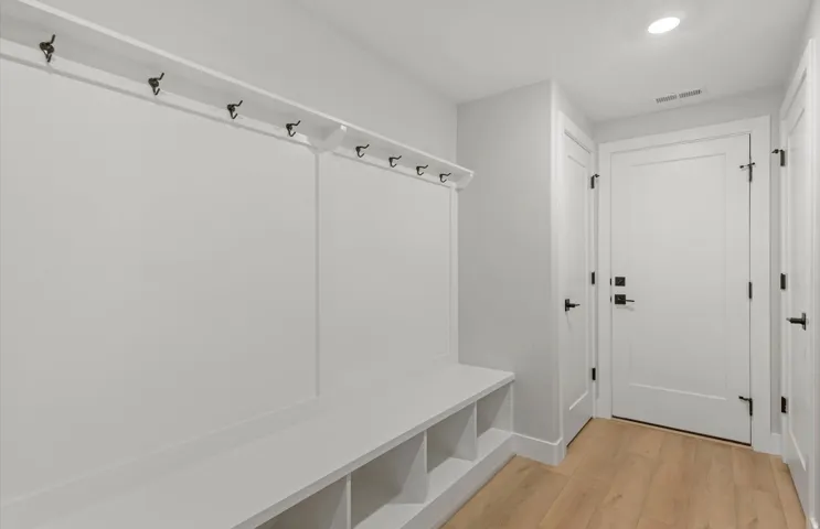 Built-in storage bench with cubbies, multiple coat hooks, wood-finish flooring, and recessed ceiling lighting