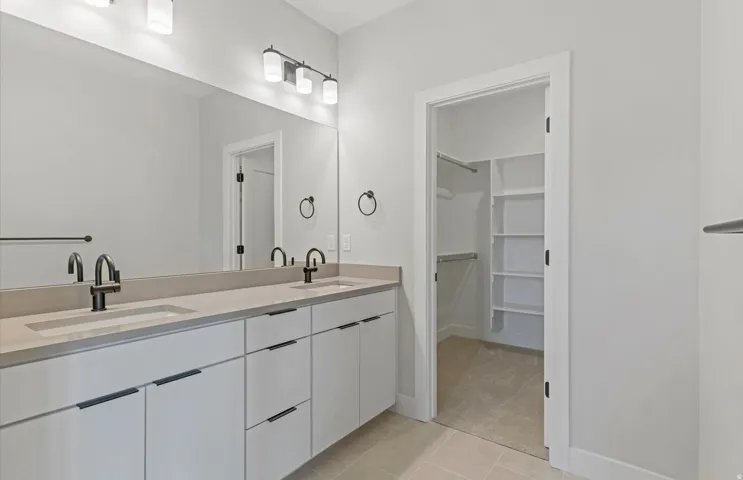 Owner's bath featuring dual basin vanity with matte black fixtures, integrated sinks, extended mirror, and built-in closet shelving