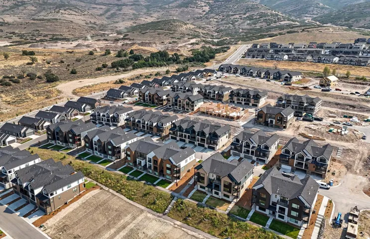 New construction residential development featuring multi-story residences with dark pitched roofs, light siding, and mountain backdrops