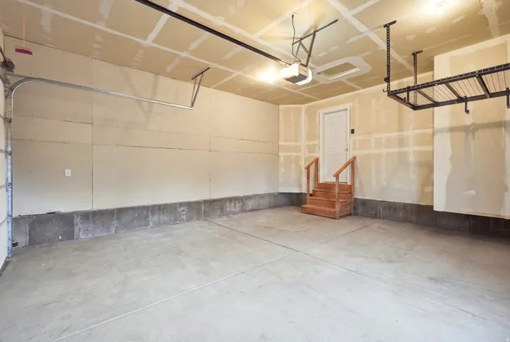 Concrete flooring, overhead lighting, automatic garage door opener, wooden interior steps, and an overhead storage rack