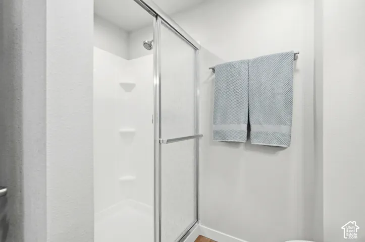 Shower with a sliding glass door, white shower surround, multiple built-in shelving units, and a chrome shower head