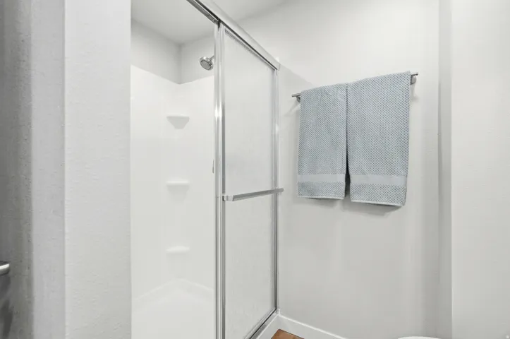 Shower with a sliding glass door, white shower surround, multiple built-in shelving units, and a chrome shower head
